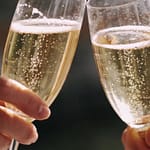Champagne Laurent-Perrier: storia, stile e segreti di una Maison iconica tra prestigio e innovazione 1 un close up molto stretto su mani che reggono calici di vino frizzante giallo paglierino tenue mentre brindano